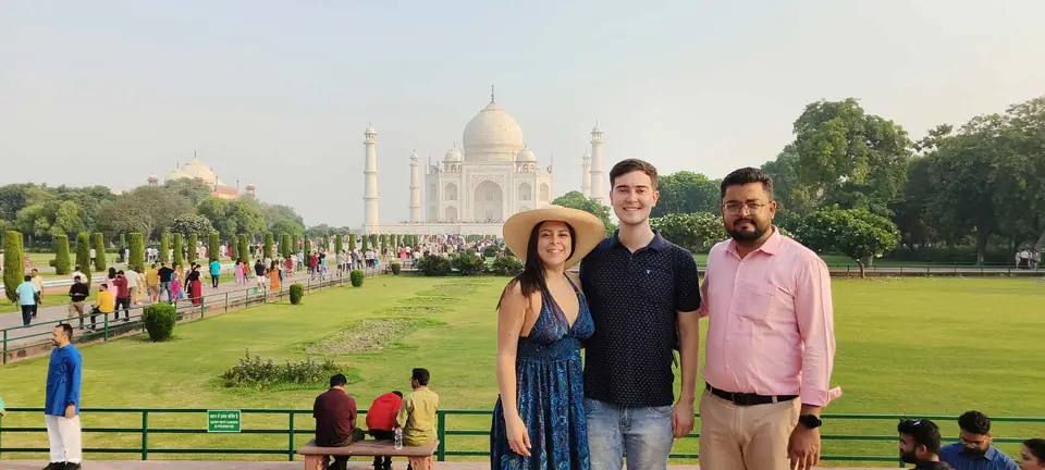 Three travellers posing in the Taj Mahal gardens with the mausoleum behind them