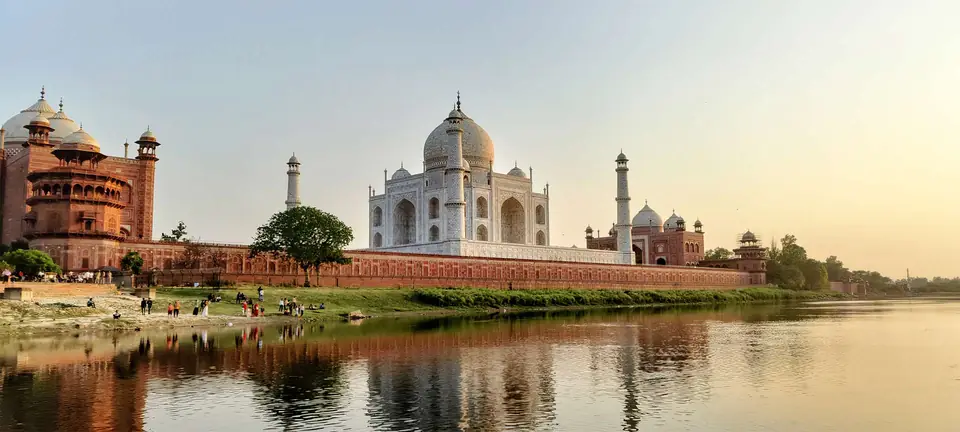 The Taj Mahal and its red sandstone mosque reflected in the Yamuna river at sunset
